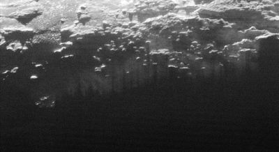 Shafts of sunlight pouring through gaps in mountains on Pluto shine through low-lying haze, or "fog," in valleys and plains.
