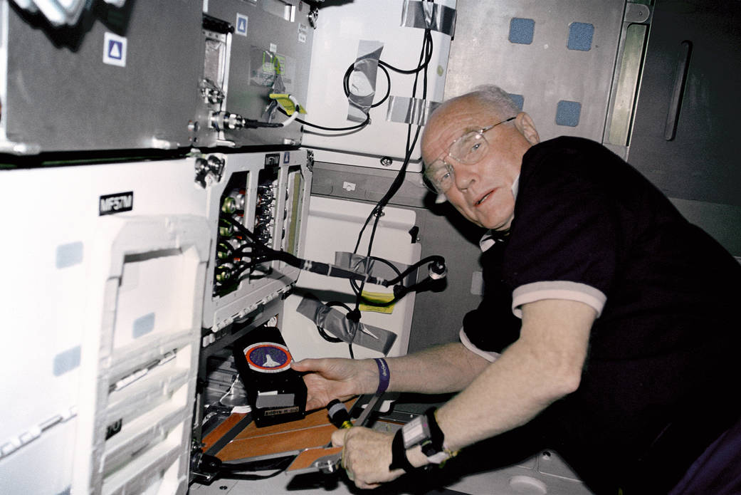 STS-95 payload specialist John Glenn works with the Osteporosis Experiment in Orbit (OSTEO) experiment located in a locker in the Discovery's middeck.