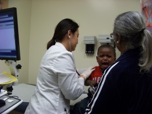 At the Manual Arts High School Wellness Center in Los Angeles, pediatric nurse practitioner Jennie Lien gives 15-month-old Andrew Baptist a medical examination. Andrew's great-grandmother, Yvonne Lee (right) says Andrew's entire family relies on the center for medical care.(Photo/Chris Richard)