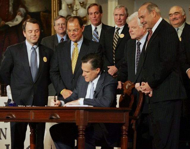 Mitt Romney, as governor of Massachusetts, signs the state's health care reform bill into law in April, 2006. Sen. Ted Kennedy (2nd from right) and others look on. ( Joe Raedle/Getty Images)