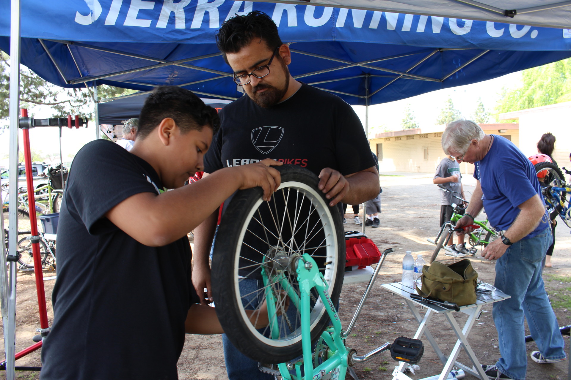 Jaime Rangel, 26, helps Gustavo Ruiz, 12, fix the flat tire on his bike at the Mosqueda Community Center park. Rangel says he makes a point of showing kids and adults who may not have funds to repair their bikes at a shop, how to fix their bikes on their own. 