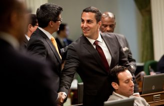 Two men in dark suits with ties shake hands in the California Assembly.