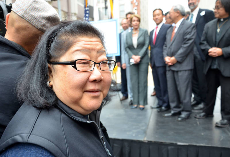 A Chinese woman with glasses looks at the camera with people in the background.