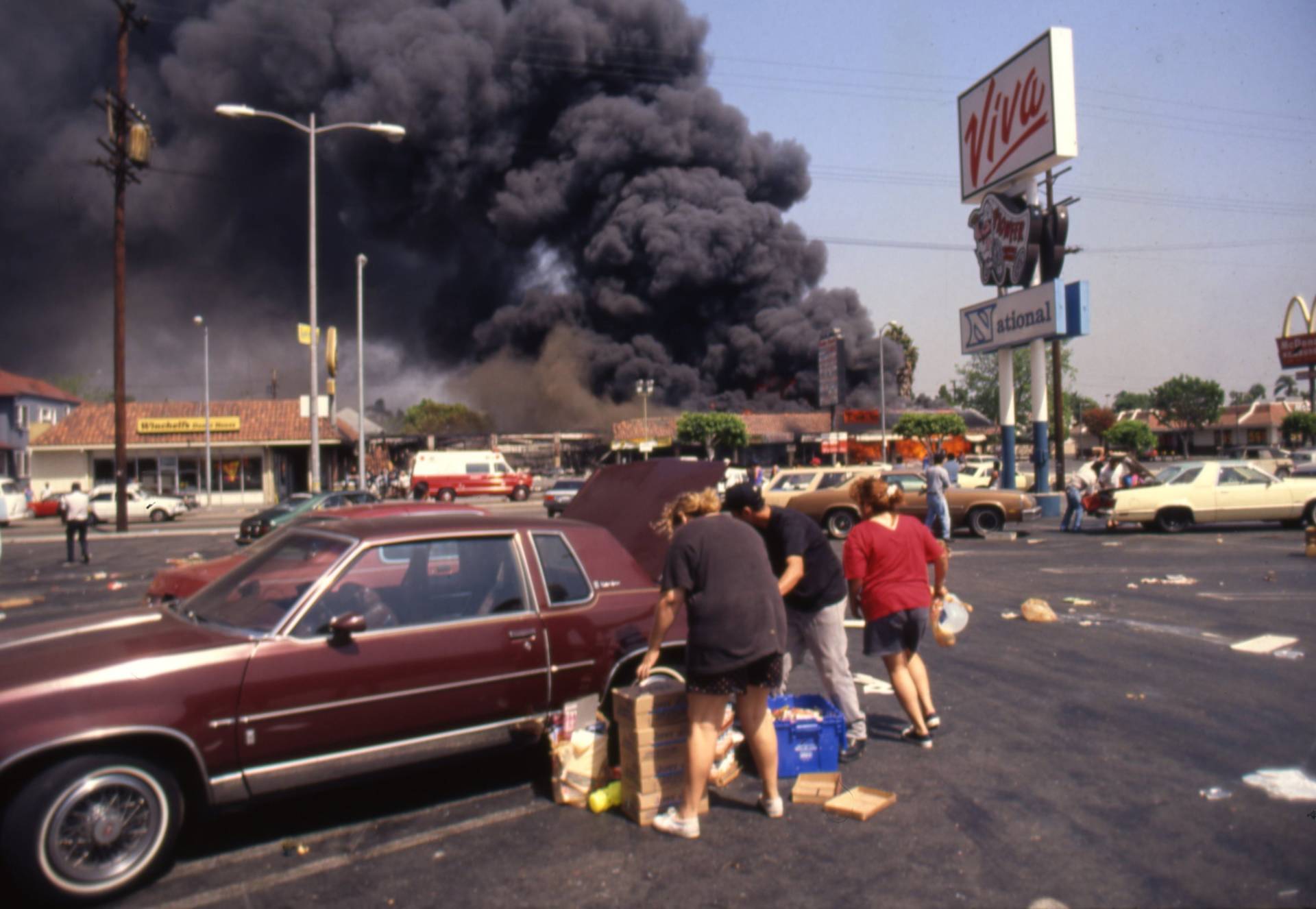 Looters load up a car at the Viva shopping center near a billowing fire during the rioting that erupted in Los Angeles on April 29, 1992, after a jury found four Los Angeles Police Department officers not guilty in the beating of Rodney King. Ron Eisenbeg/Michael Ochs Archives/Getty Images