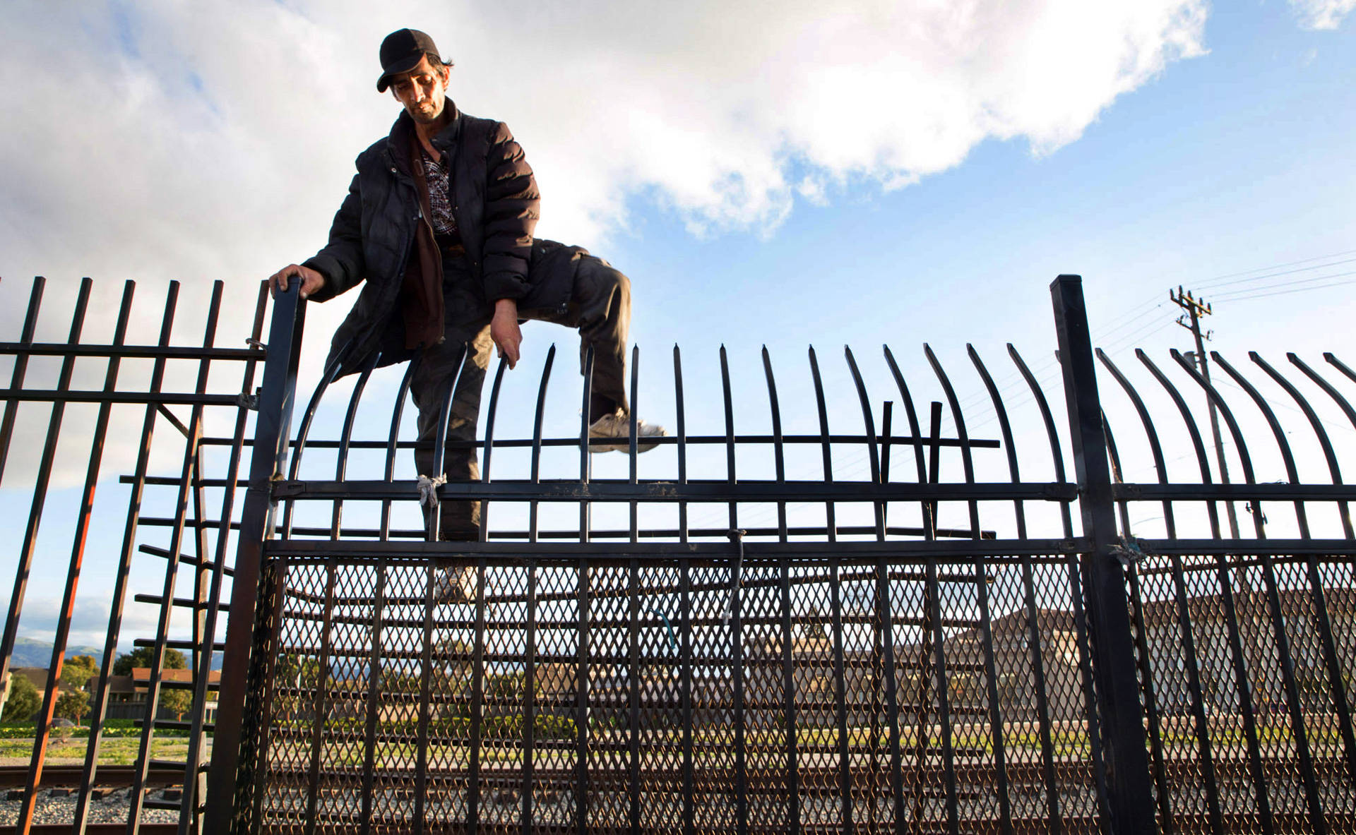 A man climbs over a fence bordering the railroad tracks that separate Chinatown from the rest of downtown Salinas. It's a common route for many Chinatown residents since accessible walking routes in and out of the neighborhood are scarce. Sarah Craig/KQED