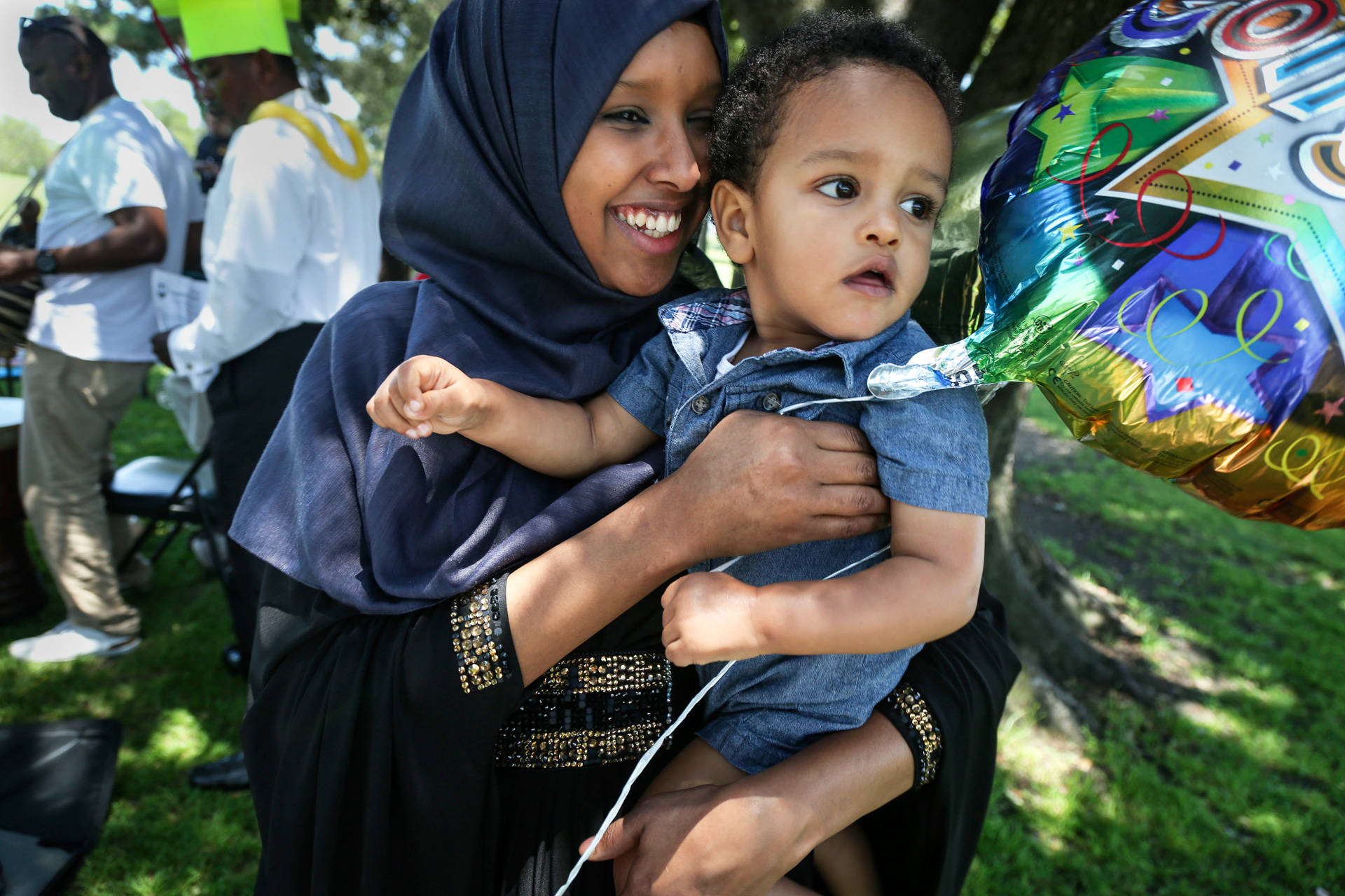 Anisa Omar holds her friend's son while his mother dances at a picnic where primarily Congolese refugees celebrate completion of English classes. Peggy Peattie/CALmatters