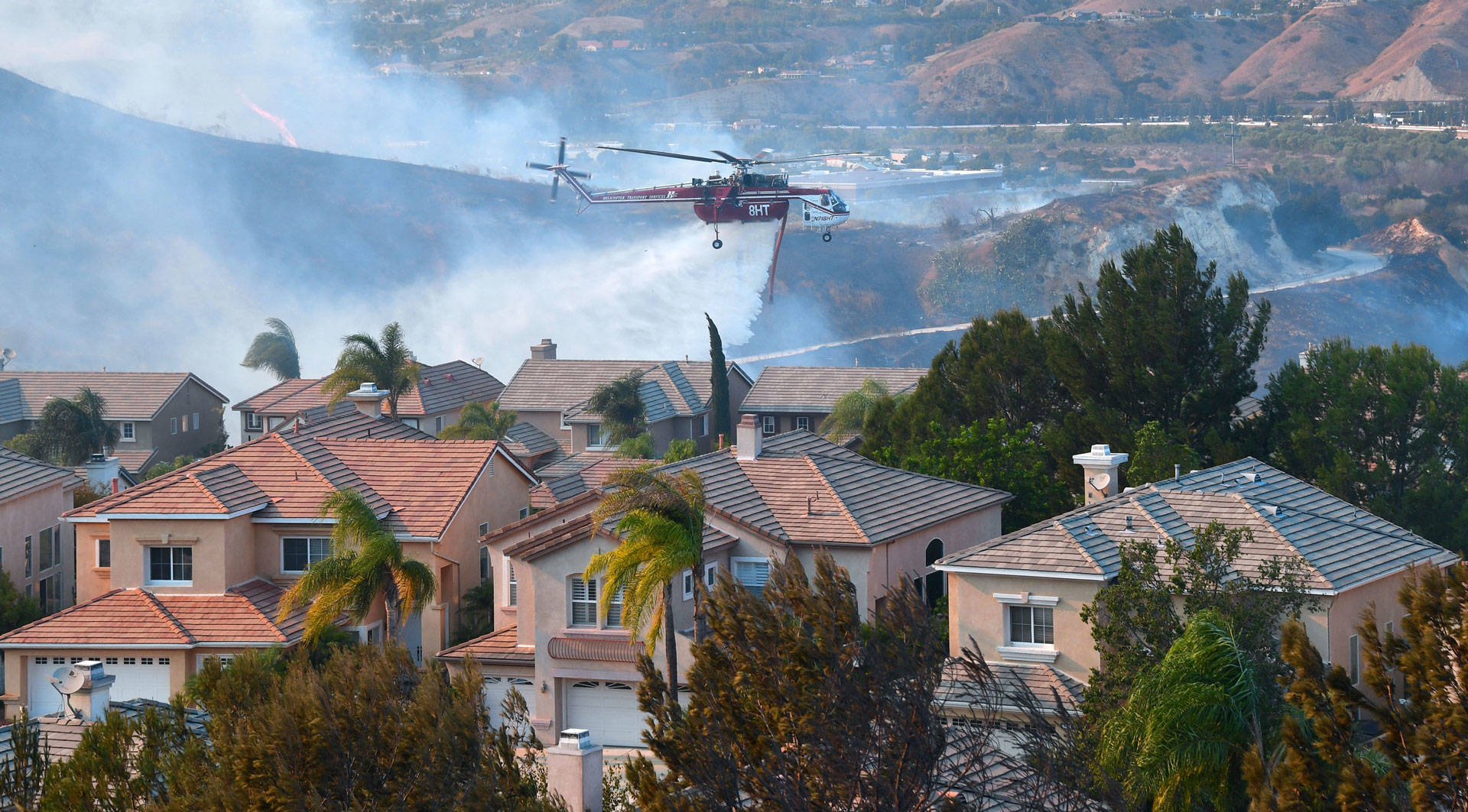 A helicopter drops water near homes at the Anaheim Hills neighborhood in Anaheim on Oct. 9, 2017, after a fire spread quickly through the area prompting mandatory evacuations and freeway closures. FREDERIC J. BROWN/AFP/Getty Images