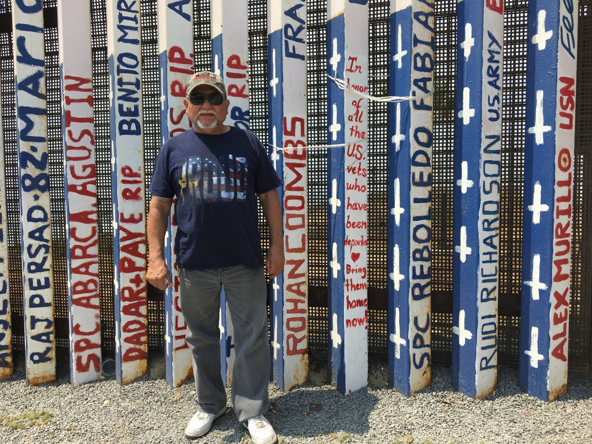 Jose Cardenas, 67, stands at U.S.-Mexico border fence in Tijuana that has been painted with the names of deported U.S. veterans. Cardenas was drafted into the U.S. Army in 1970, served seven years in the U.S. military and was deported in 2009 after a drug conviction.  Erika Aguilar/KQED News
