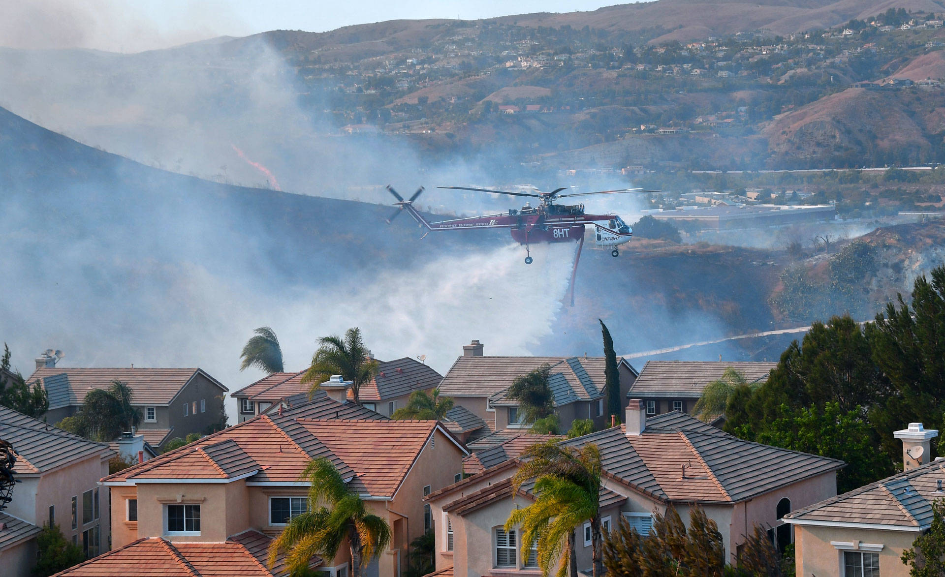 A helicopter drops water near homes in the Anaheim Hills neighborhood on Oct. 9, 2017. Orange County experienced rapid growth in housing construction in fire-prone areas between 1990 and 2010. FREDERIC J. BROWN/AFP/Getty Images
