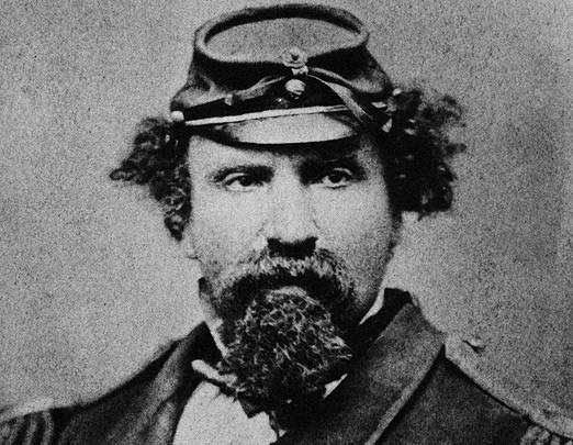 A black-and-white photo of a man with puffy hair and a puffy beard wearing a Civil War-era cap.