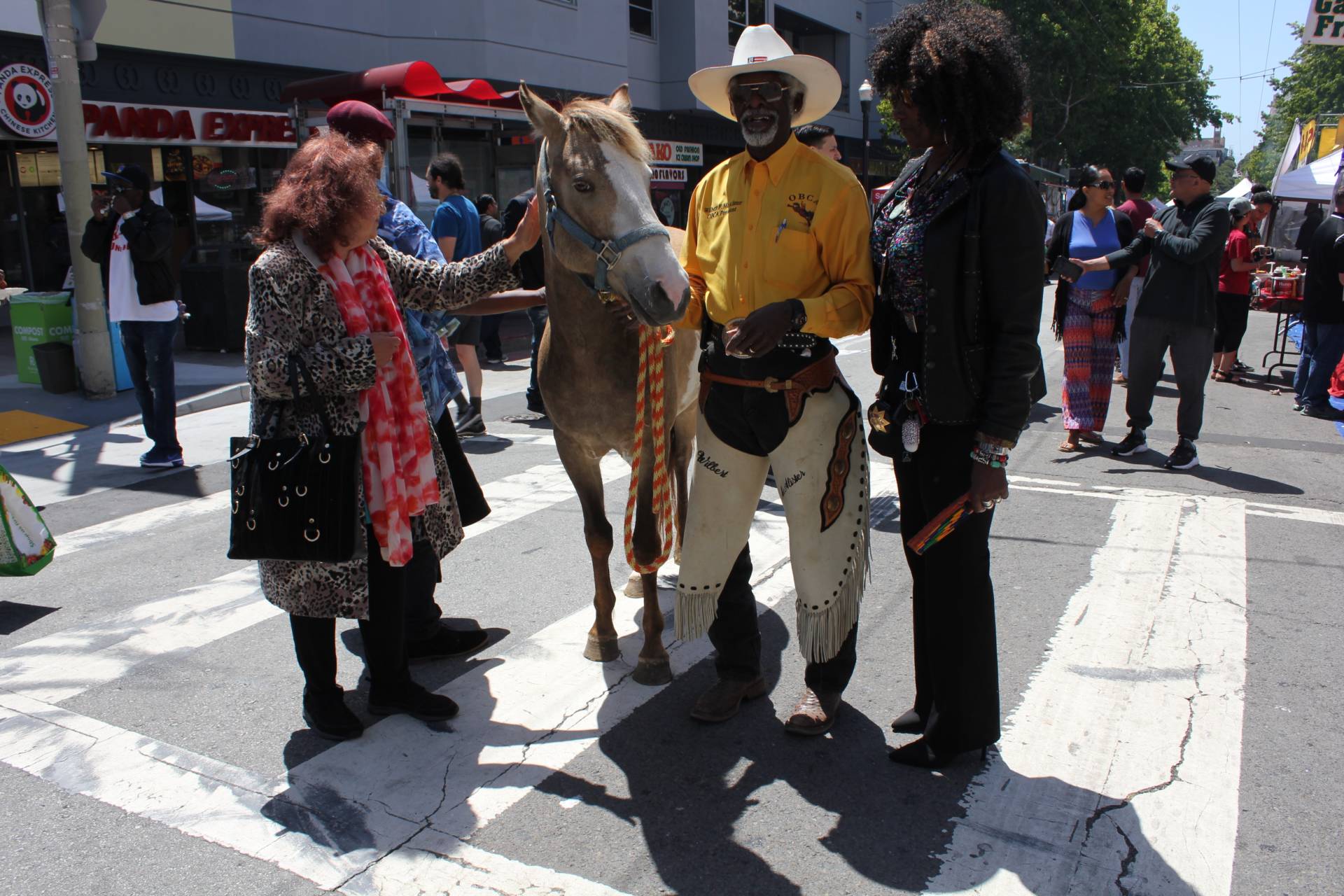 Wilbert McAllister President of Oakland Black Cowboys Association introduces pony, Martin Luther, to San Francisco Juneteenth-attendee Irina Dalian alongside Yolanda Williams of the San Francisco Police Officer's Association. McAllister says Martin Luther is here to honor "fallen cowgirl" Rachel Townsend, longtime event organizer who passed away earlier this year.