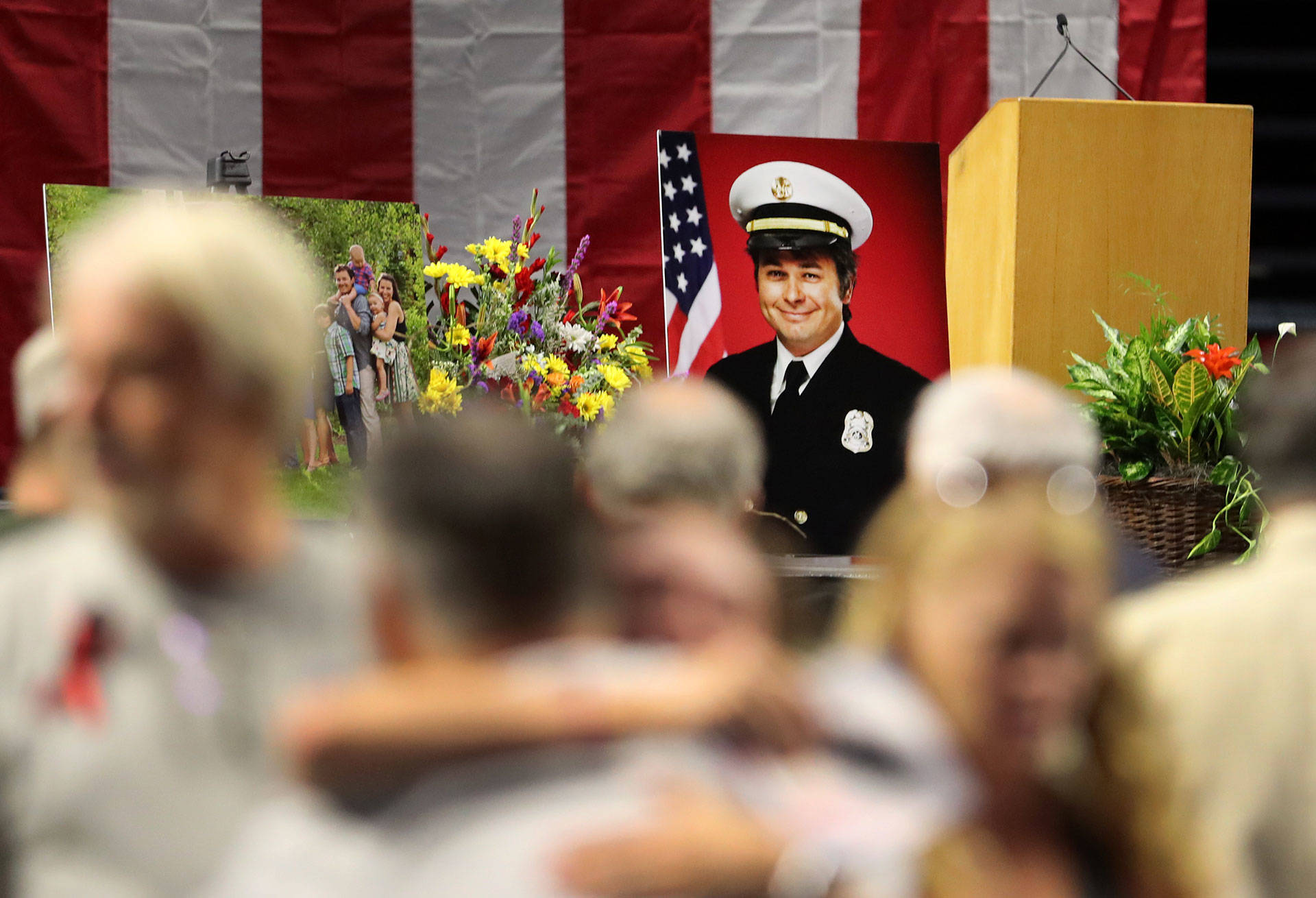 A picture of Battalion Chief Matthew David Burchett, killed battling the Mendocino Complex Fire, sits on stage as mourners embrace before his funeral on August 20 in West Valley City, Utah. George Frey/Getty Images
