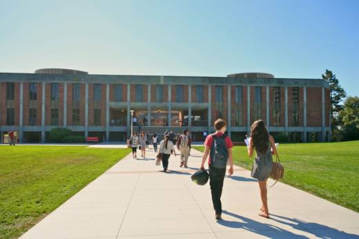 Students walk down a path through lush lawns toward a two-story building on a clear sunny day with blue skies.