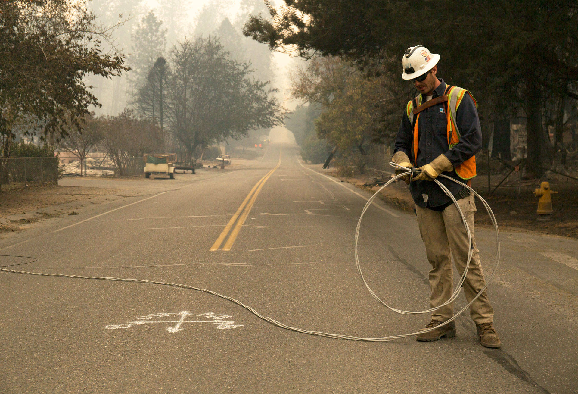 A PG&amp;E worker clears fallen power cables from a road in the Butte County town of Paradise after the Camp Fire swept through the community in November 2018.  Anne Wernikoff/KQED