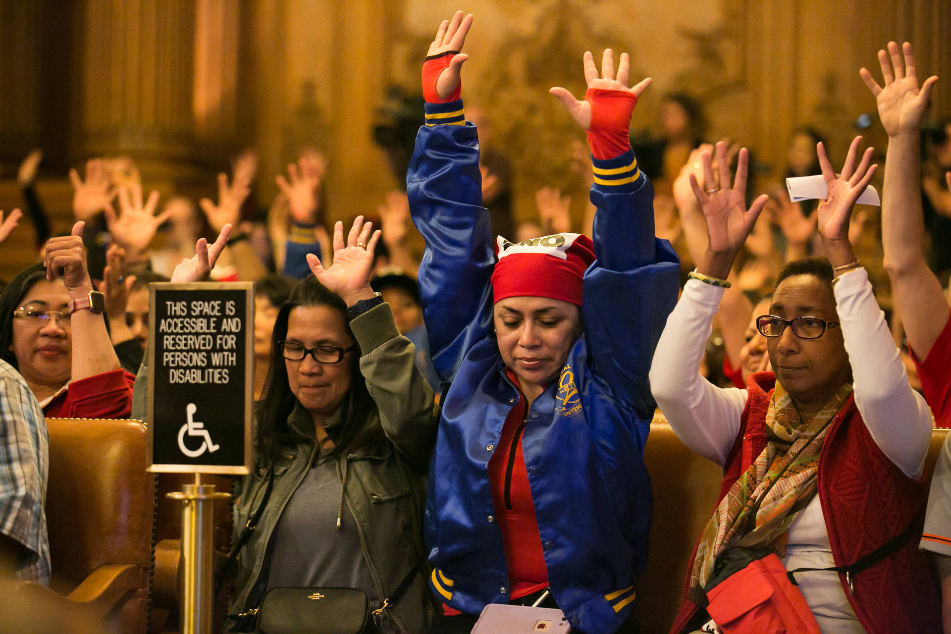Camucha King (middle right) and Nicole Drysdale (right) gesture in affirmation to a speaker during the public comment section of the San Francisco Board of Supervisors meeting on Nov. 2, 2018. King and Drysdale work at the St. Regis hotel in the food and beverage department. J.P. Dobrin/KQED