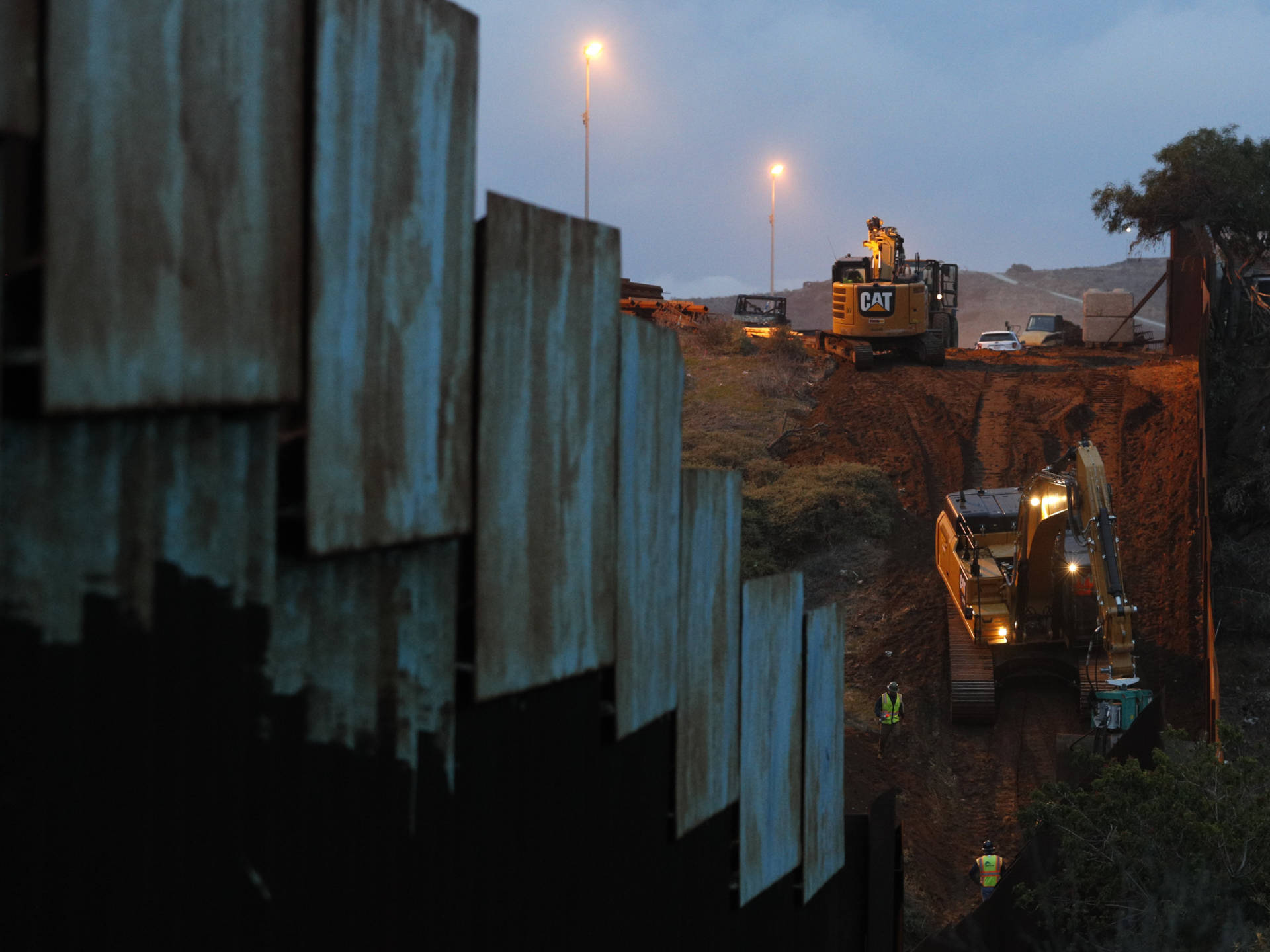 Contractors work to reinforce a section of the U.S. border wall in San Diego where scores of Central American migrants have crossed illegally in recent weeks, photographed through the fence from Tijuana, Mexico. Rebecca Blackwell/AP