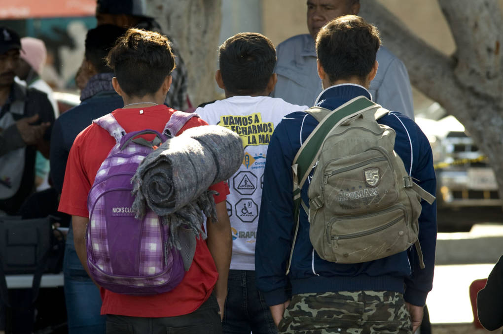 Three young men stand in line to add their names to a waiting list for people seeking asylum on Nov. 21, 2018, in Tijuana, Mexico. David Maung/KQED