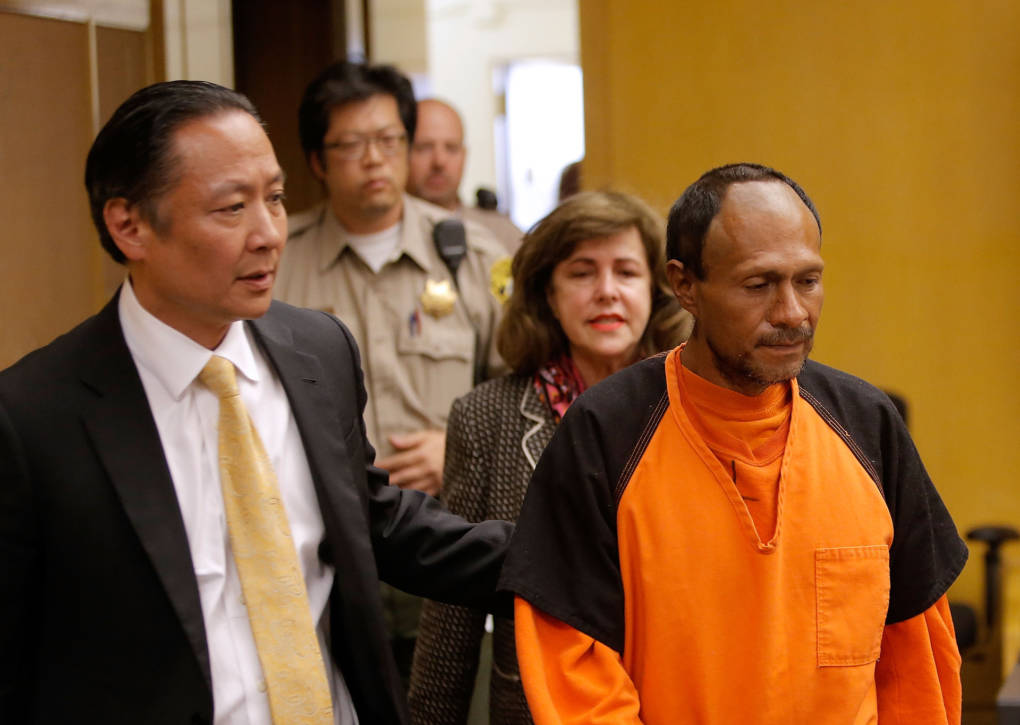 A man in a suit and tie leads another man in an orange jumpsuit into court.