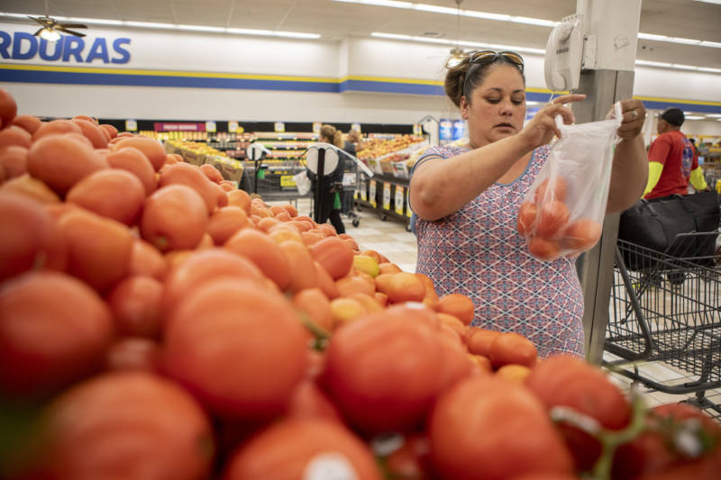 A woman holds up a plastic bag with tomatoes in a grocery store.