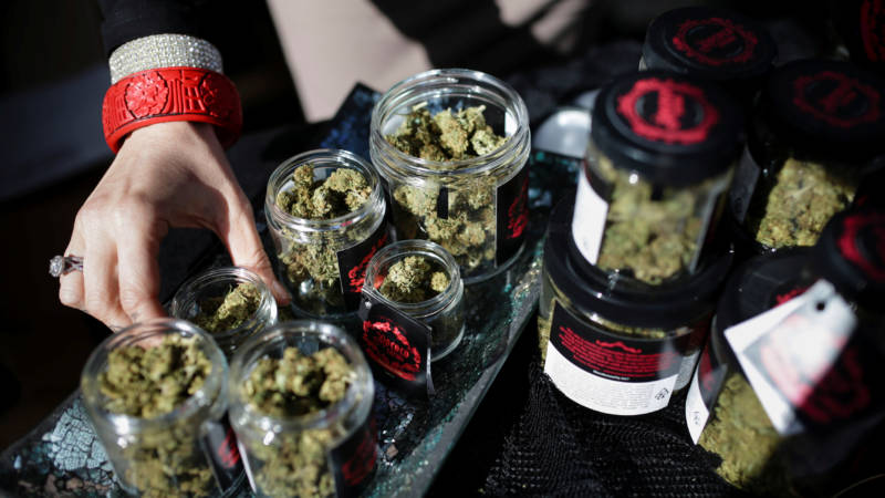 Glass jars filled with marijuana plant buds are lined up on a table.