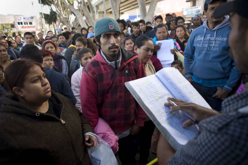 People listen as a man calls out the names on a waiting list whose turn it is to walk to the U.S. border crossing in Tijuana where they will then ask for asylum.