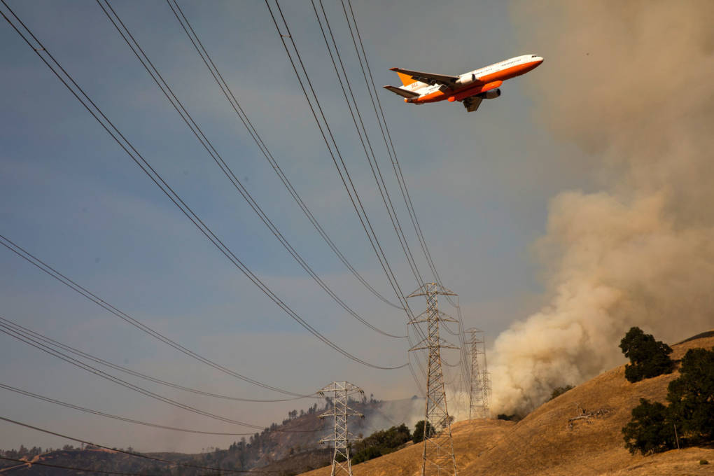 A jet air tanker flies over smoky hillside and power lines during 2019 Kincade Fire.