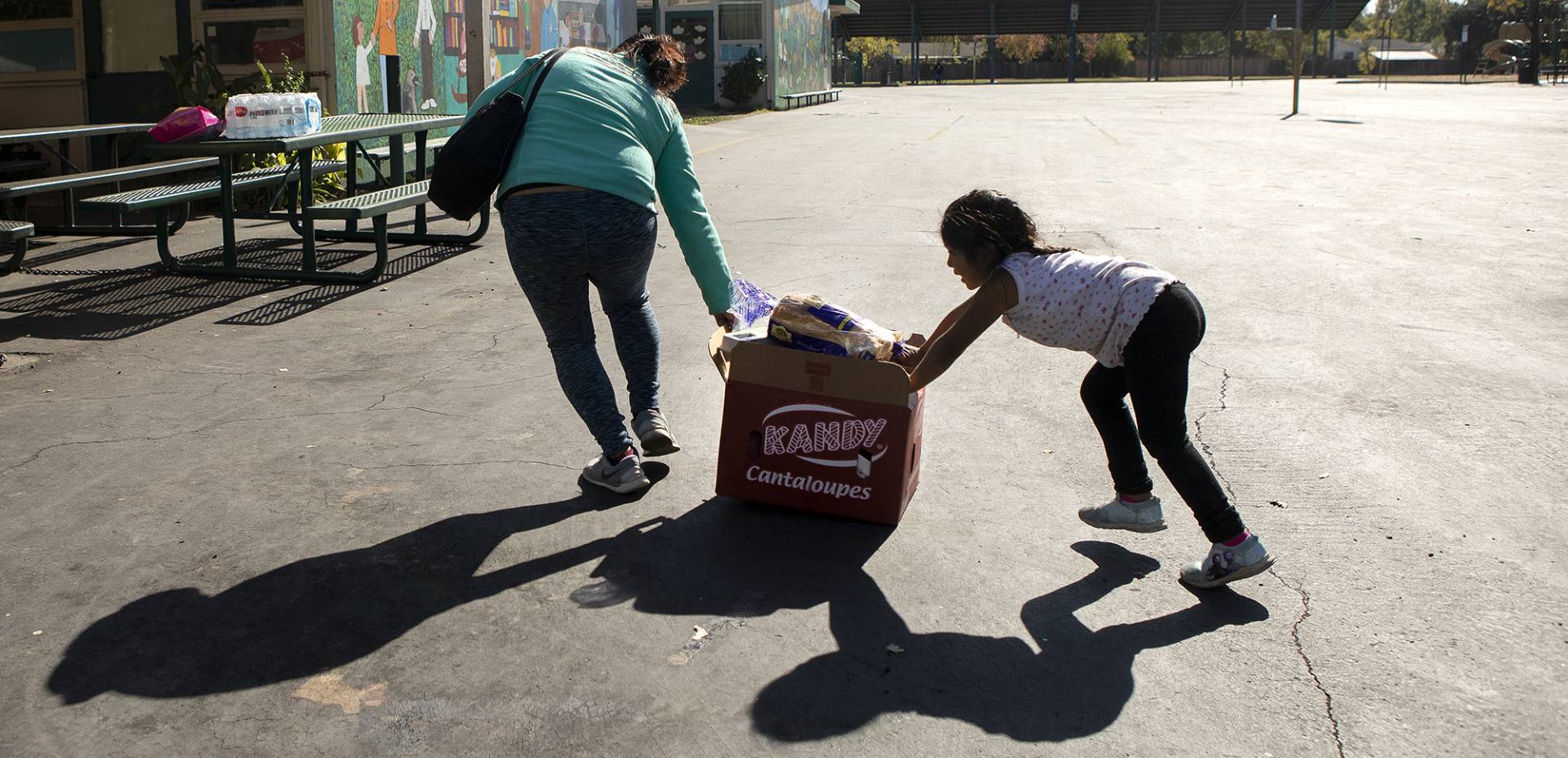 A mother and daughter push a crate of food across the yard at El Verano Elementary School during a food distribution for families affected by October's planned power outages.  Anne Wernikoff for CalMatters