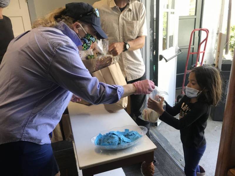 Niah Gerard, una de las organizadoras de la despensa de alimentos, le da una bolsa de comida a una niña que vino a hacer fila con su familia.