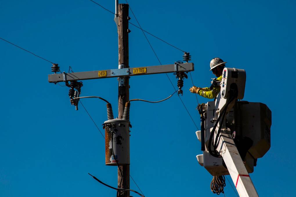 A worker in a cherry-picker working near the top of a utility pole.