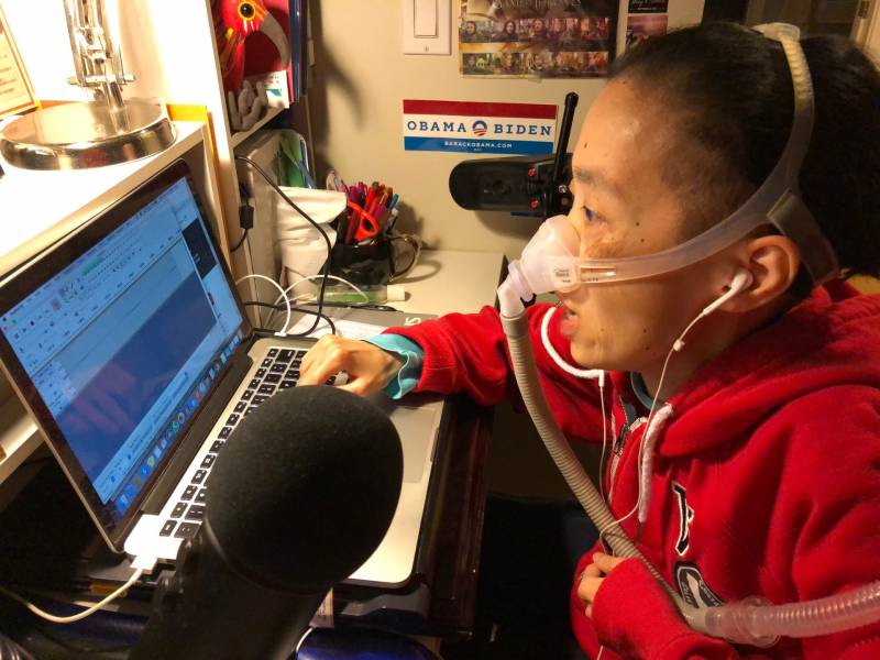 Disability rights activist Alice Wong podcasting at her desk at home.