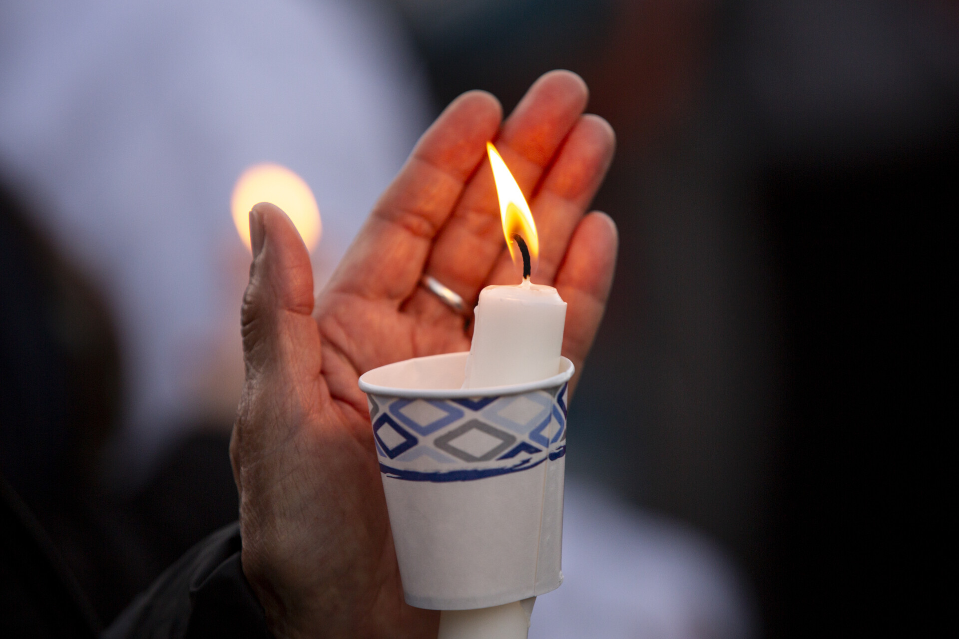 A hand hovers over a lit candle that is inside a paper cup.