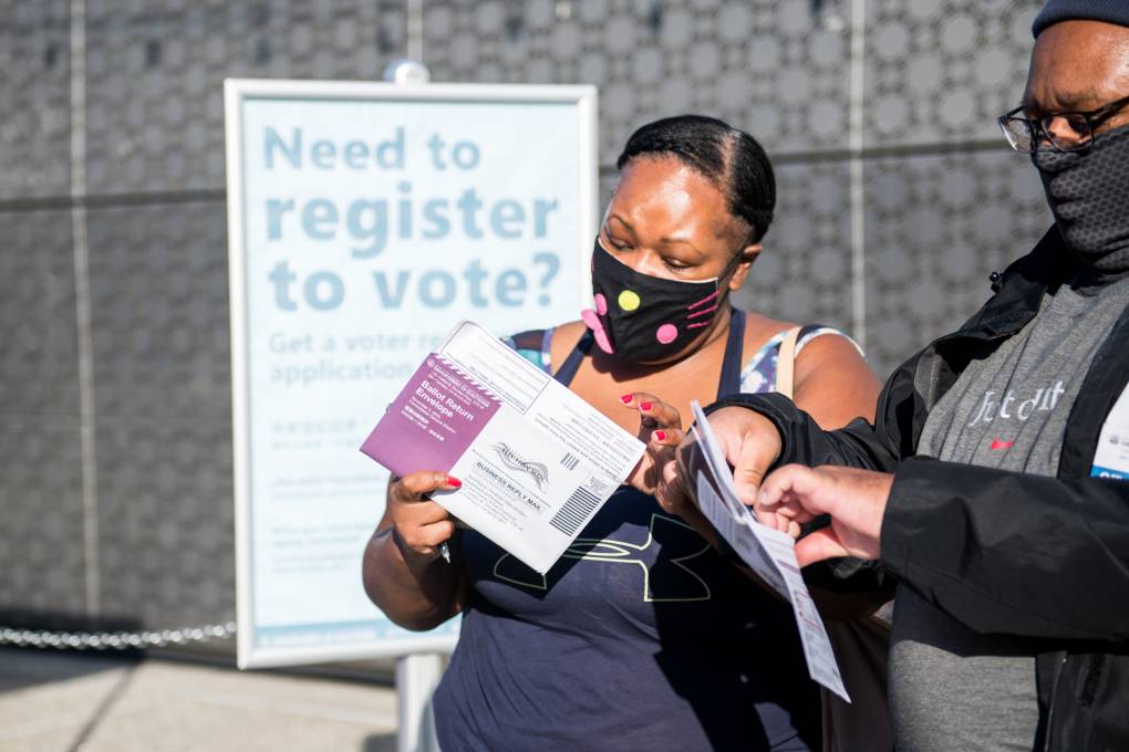 A woman and a man, both wearing face masks, examine their election ballots.