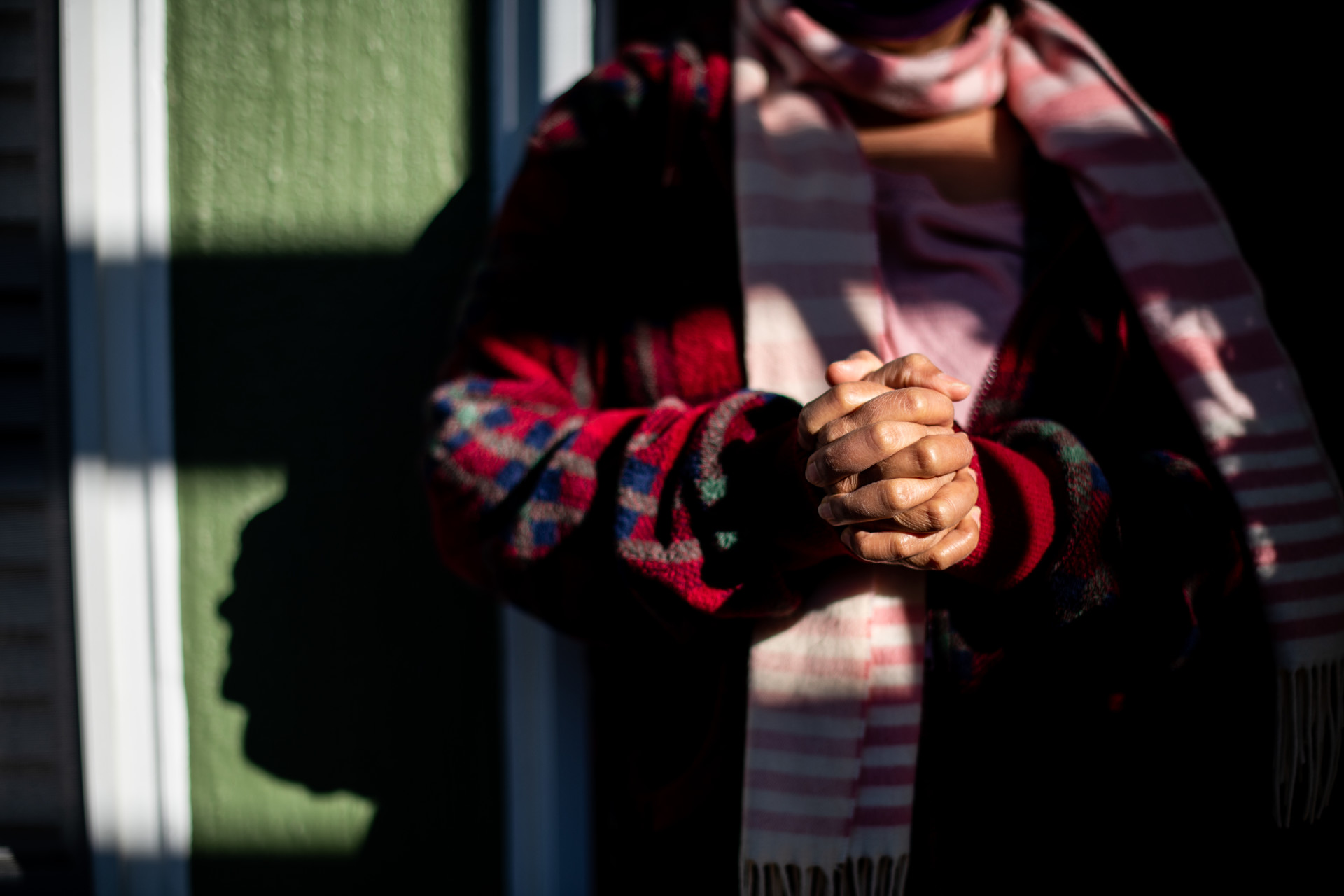 A person standing outside of an apartment building, clasping their hands together
