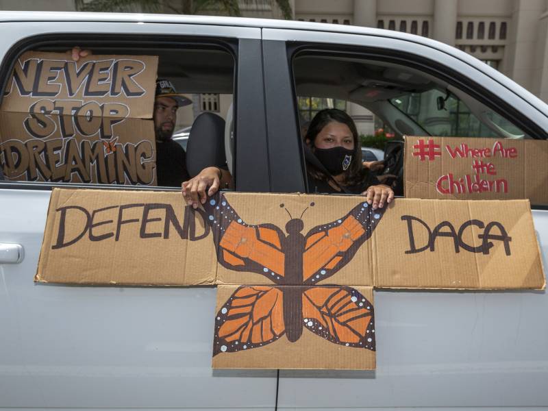 A family in a car holds signs that read 'Defend DACA,' 'Never Stop Dreaming' and '#where are the children"