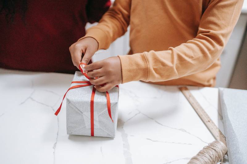 A pair of hands wrapping a white holiday gift box with red ribbon