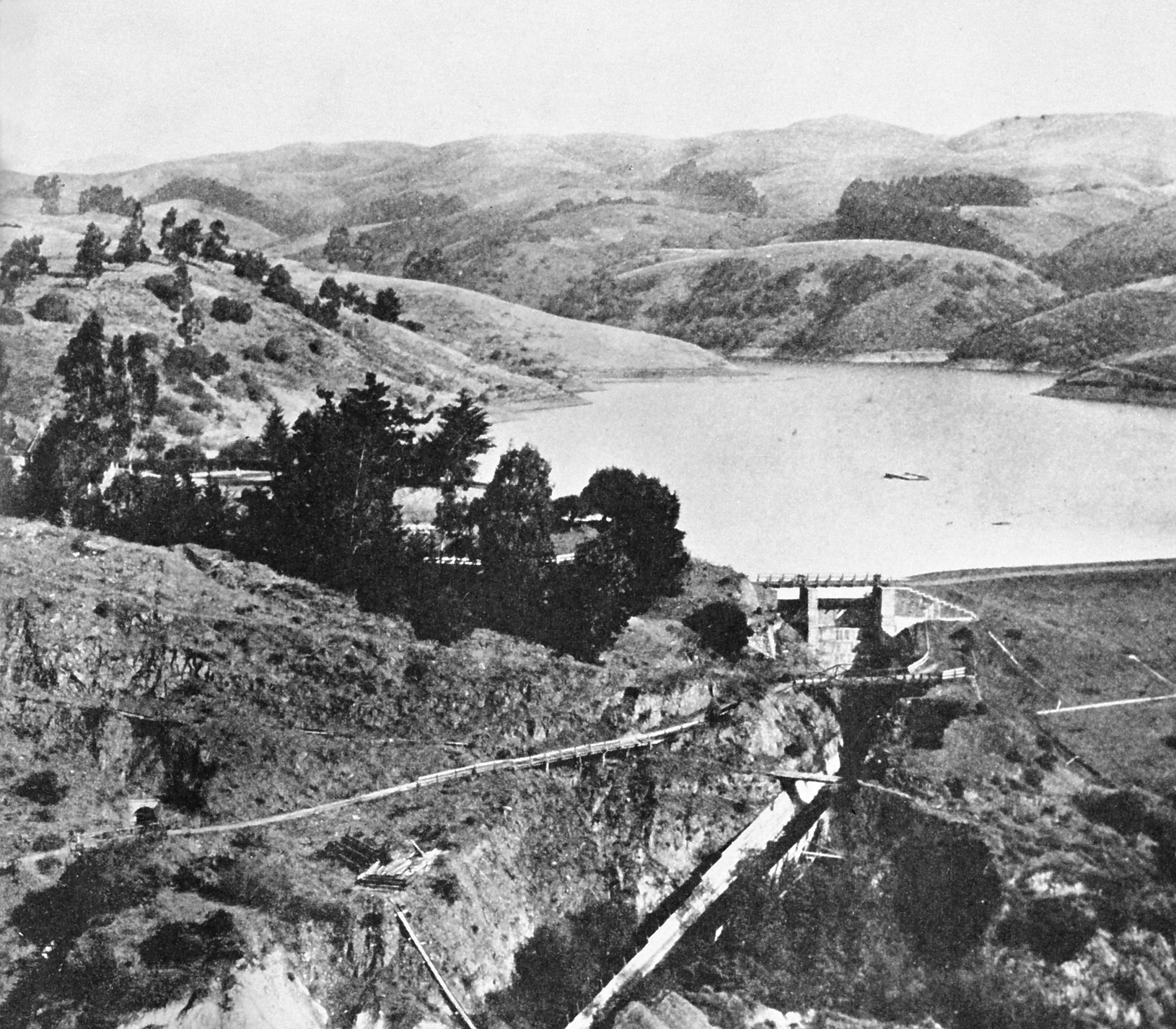 A black and white photo of lake chabot nestled below rolling hills.