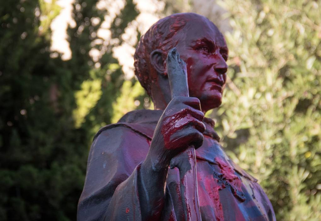 A statue of Junipero Serra holding a staff is covered in red paint