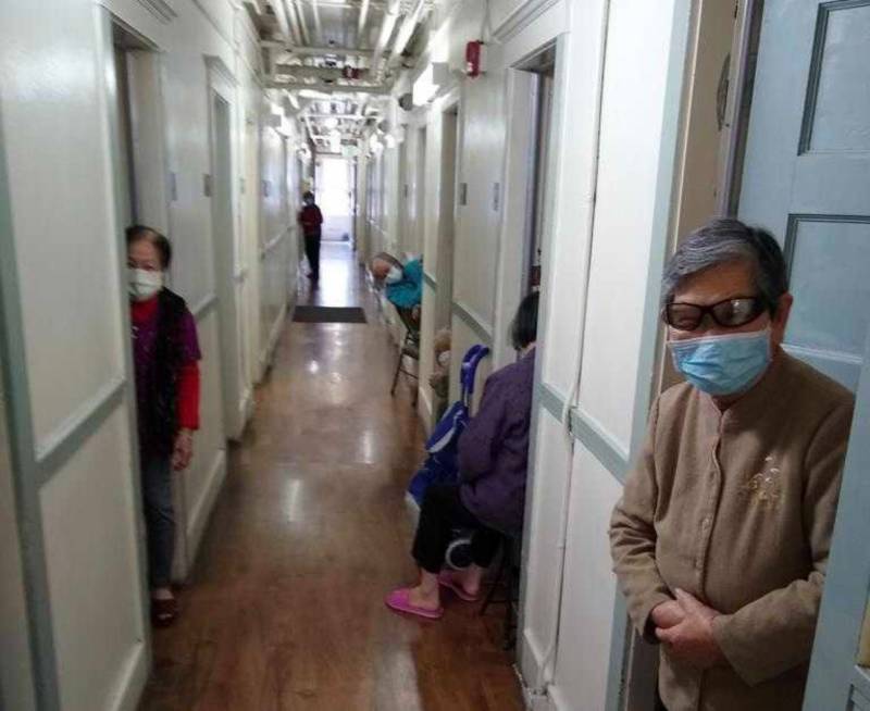 Long, spare, clean hallway with older Chinese residents standing in their doorways