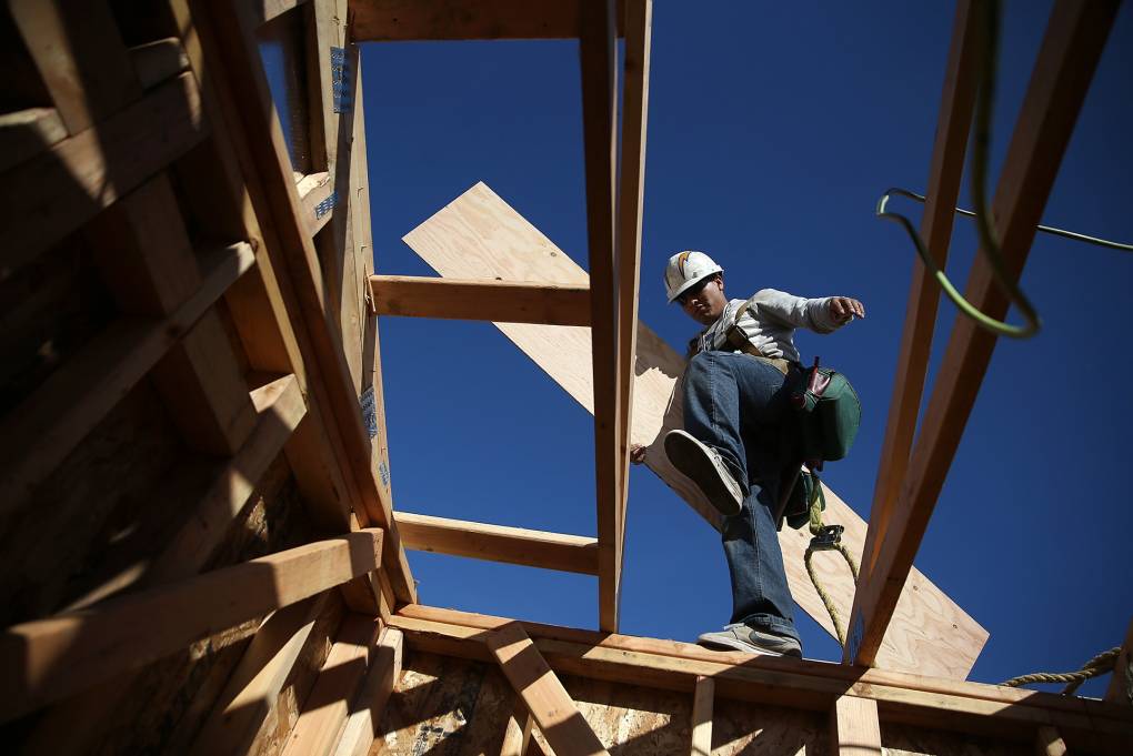 worker carrying lumber precariously on roof of building under construction