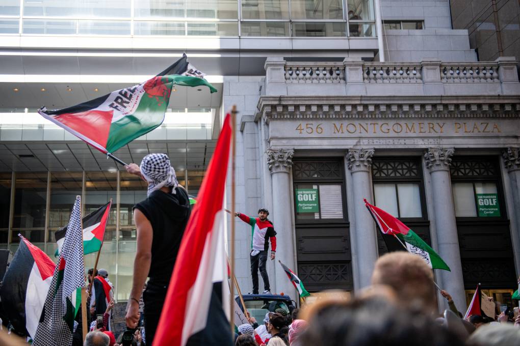 Two protesters wave Palestinian flags in front of a pro-Palestinian rally taking place outside the Israeli Consulate in San Francisco.