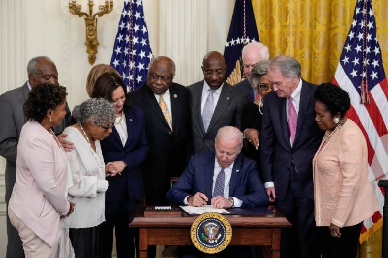 President Biden signs a document while a number of people look on.