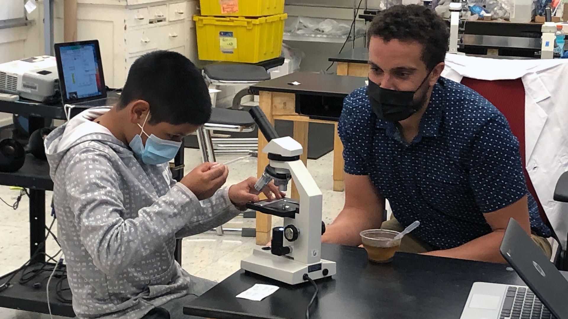 Sixth grade science teacher Patrick Messac helps a student with his microscope.