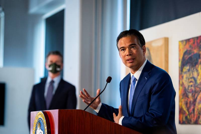 AG Rob Bonta speaks at a lectern, with Gov. Gavin Newsom standing in the background.