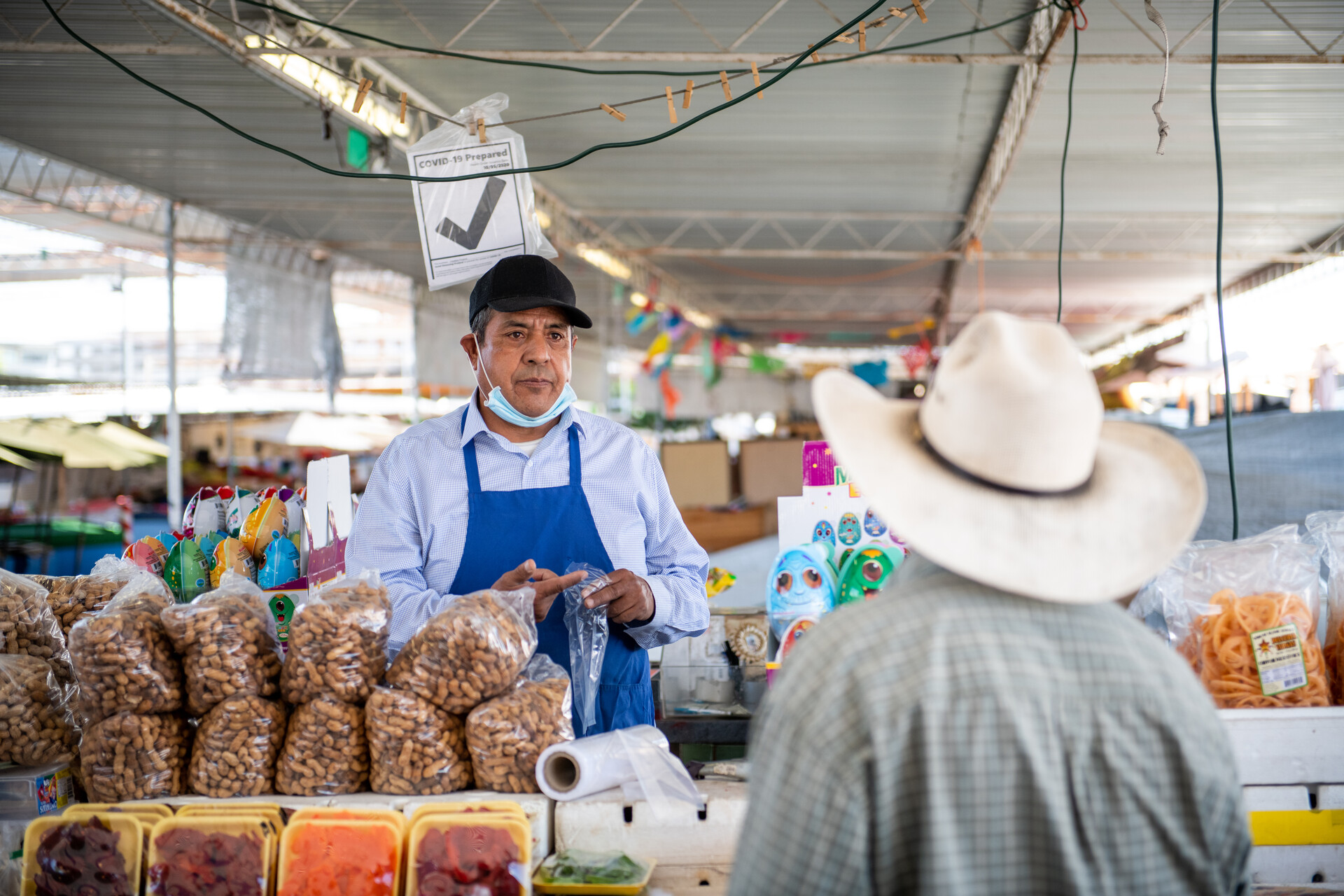 Cayetano Araújo speaks with a customer that is wearing a cowboy hat at his stall on Wednesday, May 26, 2021.