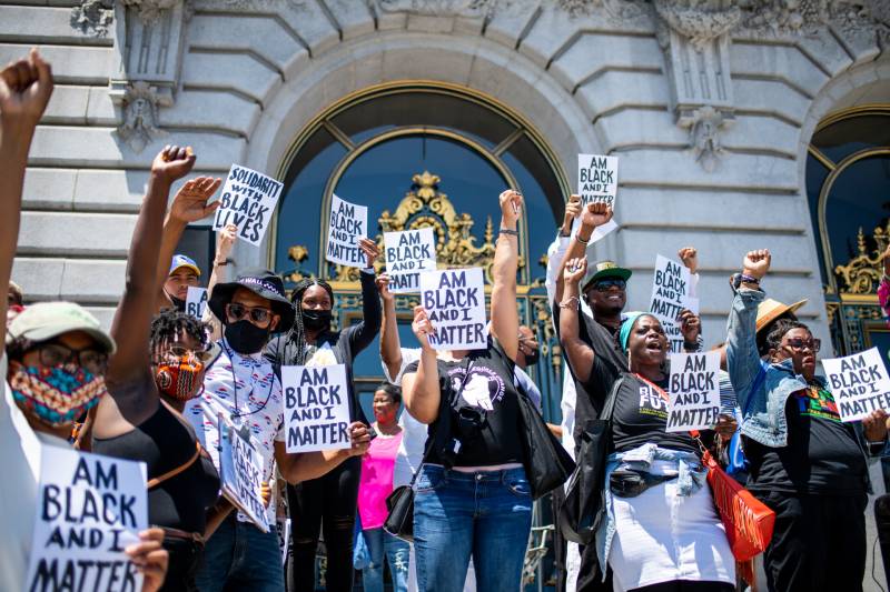 People standing in front of San Francisco City Hall hold up signs that read "Am Black and I Matter"