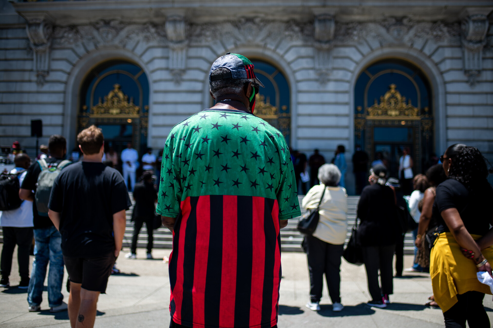 A photo of a man wearing a green, red and black shirt looking toward San Francisco City Hall