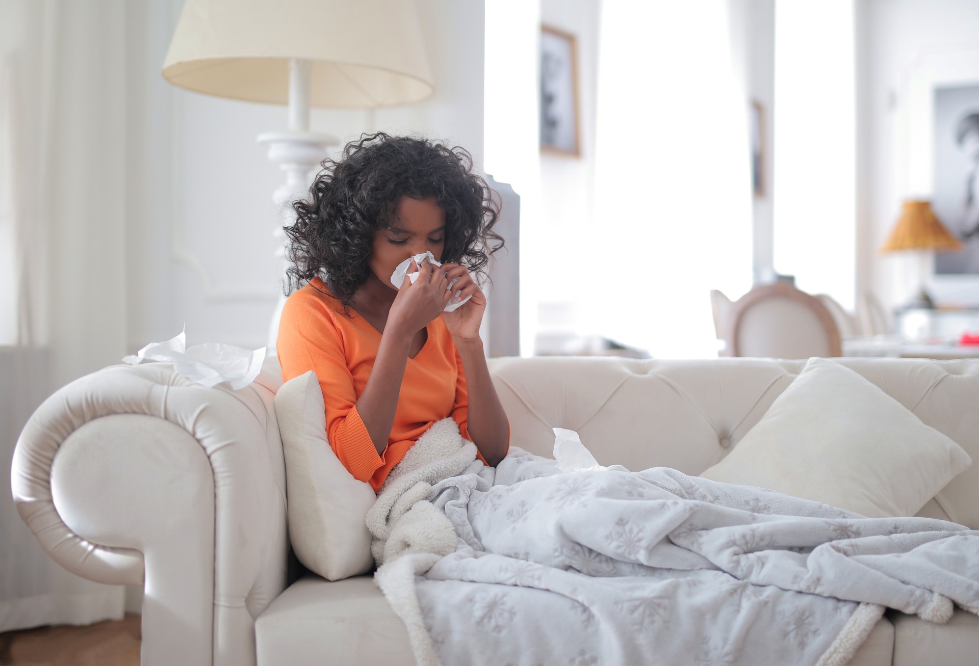 Woman on a couch wrapped in a blanket, sneezing