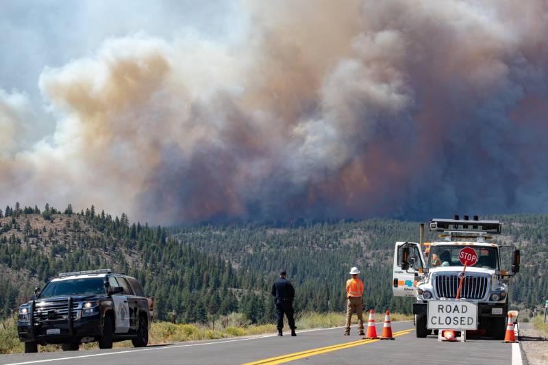 Two people stand in the middle of the road as they watch the horizon where massive plumes of smoke have grown caused by the Beckwourth Fire Complex.