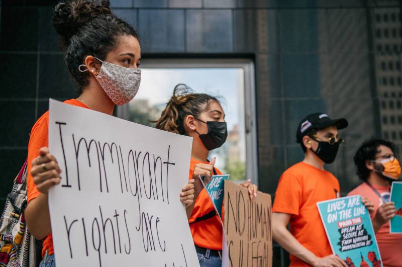 A group of youth wearing orange shirts and facemasks hold up several signs that read 'Immigrant rights are human rights.'