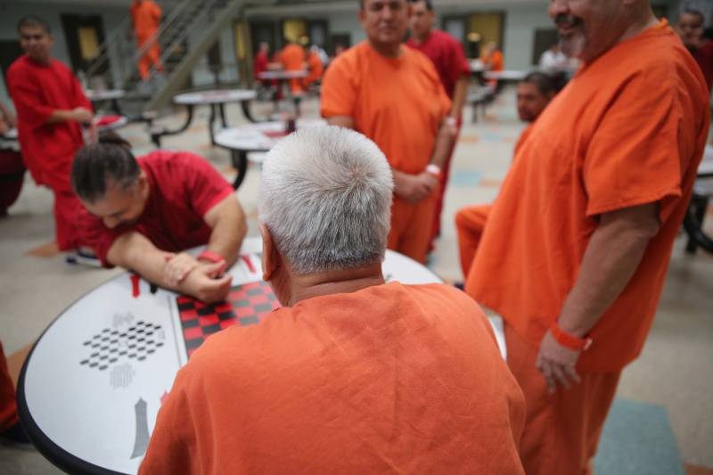 Detainees in orange jumpsuits gather around a table.
